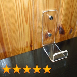 May include: A clear acrylic wall mount hook with two silver screws. The hook is mounted on a wooden wall.