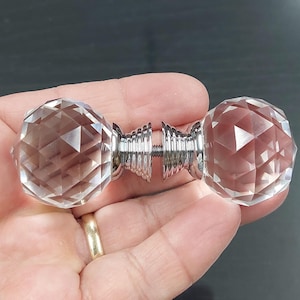 May include: A clear crystal door knob with a faceted, spherical design. The knob has a polished chrome-colored metal stem and base. The knob is held in a person's hand.