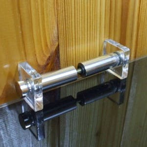 Könnte beinhalten: Eine klare Handtuchstange aus Acryl und Chrom mit quadratischen Endstücken. Die Stange ist auf einer dunklen Oberfläche vor einer Holzwand montiert. Das Logo "HiProgress" befindet sich in der oberen linken Ecke.