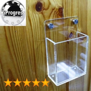 May include: A clear acrylic wall mount display stand with two silver screws. The stand is mounted on a wood panel.