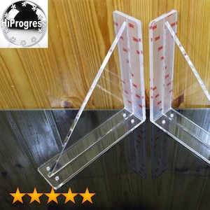 May include: Two clear acrylic shelf brackets with a 90-degree angle. The brackets are designed to support shelves and have a smooth, polished finish.