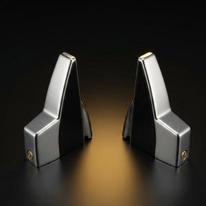 May include: Two symmetrical, angular metal components with a polished silver finish and black side panels. Each piece features a distinct, tapered vertical shape with a small circular gold-toned screw or fastener visible on the lower side section.