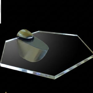 May include: A hexagonal clear acrylic shelf with a smooth, reflective surface. The shelf is attached to a single, metallic, teardrop-shaped wall bracket with a polished finish. The design features clean, straight edges and a transparent appearance.