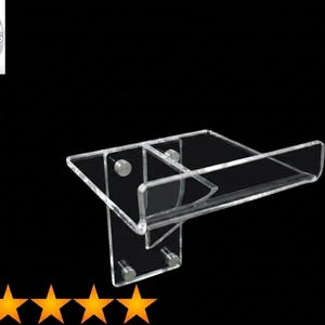 May include: A clear acrylic wall-mounted display shelf featuring a vertical back panel with four circular mounting points and a horizontal platform with a raised front edge. The design is transparent and rigid, providing a sleek surface for items.