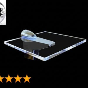 May include: A square, clear acrylic shelf featuring a polished chrome-finished metal bracket. The shelf has a smooth, transparent surface and is attached to a wall-mounted support piece. The design is simple, functional, and modern in appearance.