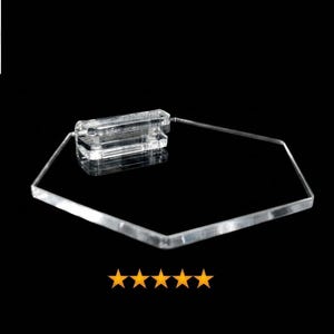 May include: A clear, hexagonal acrylic display stand featuring a rectangular base attachment. The top left corner displays a circular logo with the text HiProgress surrounded by stars, and five orange stars are positioned below the stand.