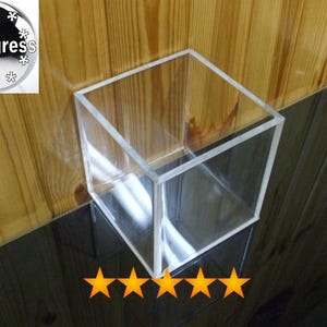 May include: A clear acrylic cube container, ideal for organising small items or displaying trinkets. The cube is sitting on a dark surface.