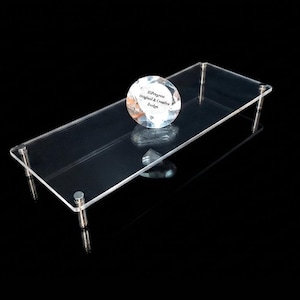 May include: A rectangular clear acrylic display riser featuring four silver-toned metal legs at the corners. A circular, faceted glass paperweight sits on the surface, displaying the text HiProgress Original & Creative Design in black lettering.
