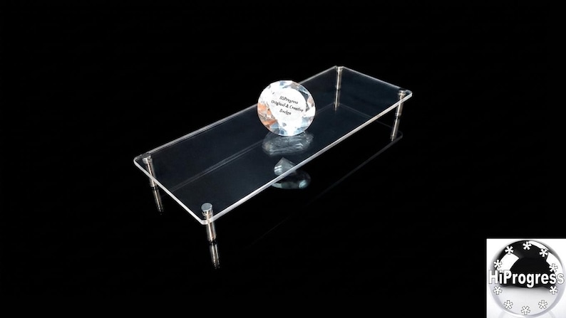 May include: A rectangular clear acrylic display riser featuring four silver-toned metal legs at the corners. A circular, faceted glass paperweight sits on the surface, displaying the text HiProgress Original & Creative Design in black lettering.