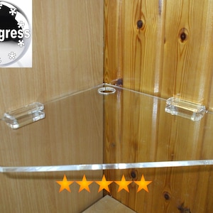 May include: Clear acrylic corner shelf with two clear plastic brackets. The shelf is mounted on a wooden wall.