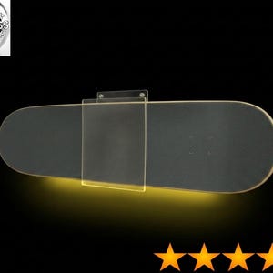 May include: A black skateboard deck mounted horizontally on a wall using a clear acrylic bracket. The setup features integrated yellow LED lighting that illuminates the area directly beneath the board, creating a glowing effect against the dark background.