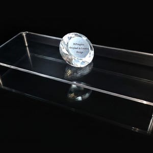 May include: A rectangular clear acrylic display riser with four silver metal cylindrical legs. Resting on the surface is a faceted clear glass diamond-shaped paperweight featuring the text HiProgress Original & Creative Design.