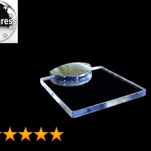 May include: A clear, square acrylic display base featuring a circular, ribbed, metallic-toned insert on its top surface. The product includes a circular logo graphic in the corner with the text HiProgress surrounded by white snowflake icons.