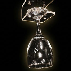 May include: A clear glass wine glass hanging upside down from a transparent acrylic rack. The rack is secured with four visible metal screws. The text HiProgress is visible in the top left corner of the image against a black background.
