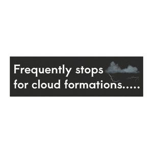 以下が含まれることがあります： 「Frequently stops for cloud formations.....」という白い文字が書かれた長方形の黒いステッカー。雲の形成の中心から稲妻が下に伸びている灰色の嵐の雲の小さなグラフィックが添えられています。