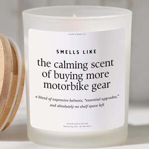 May include: A frosted glass candle with a bamboo lid. The white label reads: SMELLS LIKE the calming scent of buying more motorbike gear, a blend of expensive helmets, essential upgrades, and absolutely no shelf space left. Hand poured in the USA.