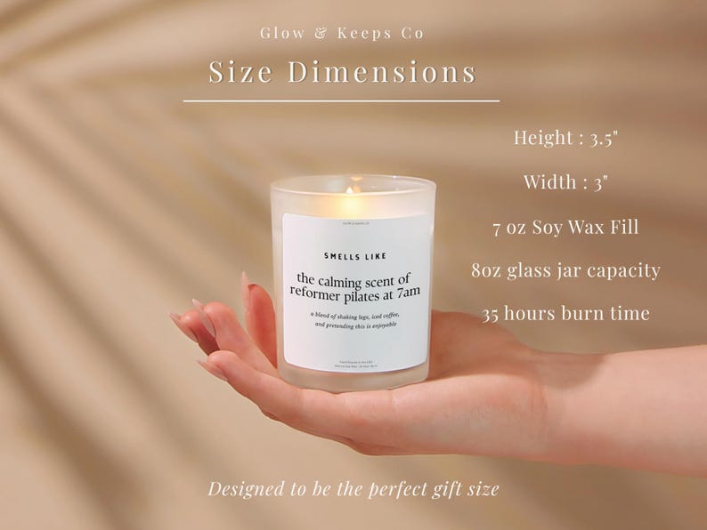 May include: A lit candle in a clear glass jar, held in a hand. The candle has a white label that reads "Smells Like the calming scent of reformer pilates at 7am." The candle is 3.5 inches tall and 3 inches wide, with a 7 oz soy wax fill and 8oz glass jar capacity.