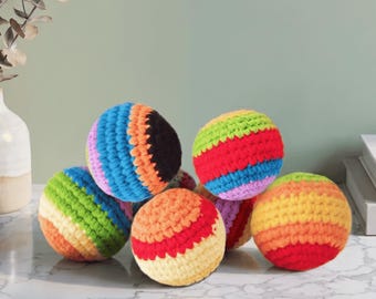 Könnte beinhalten: Sechs bunte, gehäkelte Bälle mit Streifenmustern. Die Bälle zeigen eine Reihe von leuchtenden Farben, darunter Rot, Orange, Gelb, Grün, Blau und Lila. Sie sind auf einer Marmoroberfläche angeordnet.