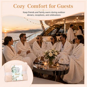 May include: A folded cream-colored ribbed blanket with a white tag featuring green leaf illustrations and the text: To have and to hold in case you get cold Thank you. The background shows people on a boat wrapped in similar blankets.