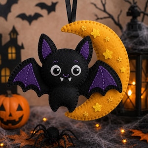 May include: A felt hanging ornament featuring a black bat with purple wing accents and white fangs, positioned in front of a yellow crescent moon decorated with small yellow embroidered stars. The ornament hangs from a black ribbon loop.