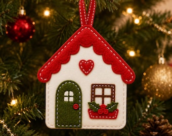 May include: A felt house-shaped Christmas ornament featuring a white facade, a scalloped red roof, and a red hanging ribbon. The design includes a green arched door, a brown window with a red flower box, and a small red heart centered above.