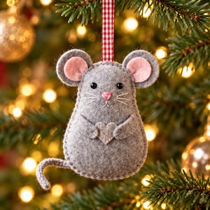 May include: A gray felt mouse ornament featuring pink inner ears, a pink nose, and black bead eyes. The mouse holds a small light gray felt heart and is suspended by a red and white checkered ribbon. The edges are stitched with gray thread.