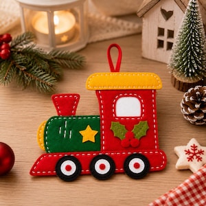 Op de afbeelding: Een kerstornament van vilt in de vorm van een trein, met een rode en groene romp en witte stiksels. De trein heeft een geel dak, een gele ster en groene hulstblaadjes met rode bessen. Het heeft drie zwarte wielen met witte centra.