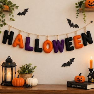 May include: A felt banner spelling HALLOWEEN in black, orange, and purple letters hanging on a string. The letters are decorated with black paper bats, orange pumpkins, a black lantern with a candle, and a book titled Spooky Season.