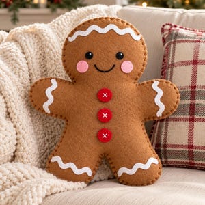May include: A brown felt gingerbread man pillow featuring white wavy icing trim on the head, arms, and legs. The face has black circular eyes, a stitched smile, and pink circular cheeks. Three red buttons with white cross stitching run down the center.