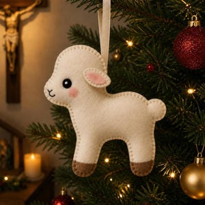 May include: A cream-colored felt lamb ornament with a light pink inner ear and cheek, dark brown hooves, and a black stitched face. The lamb is suspended by a thin cream ribbon and features a simple, soft-textured, hand-stitched design.
