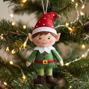 Puede incluir: Adorno navideño hecho a mano con un elfo. El elfo tiene un gorro rojo con lunares blancos, un cuello blanco y una túnica verde. El cinturón del elfo es rojo con una hebilla dorada. El adorno cuelga de una cuerda de hilo natural.