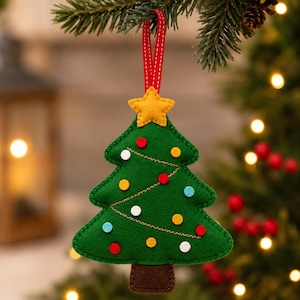 Può includere: Un addobbo natalizio a forma di albero in feltro verde con tronco marrone e una stella gialla in cima. L'albero è decorato con piccoli cerchi in feltro rossi, gialli, bianchi e azzurri, arricchiti da sottili linee di ghirlanda dorate cucite.