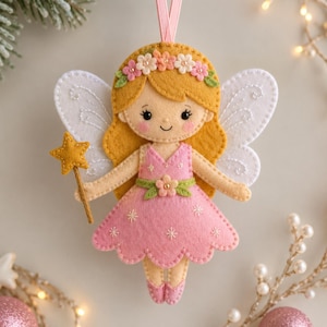 Op de afbeelding: Een vilt fee ornament met een blond figuurtje met een bloemenkrans, gekleed in een roze jurk met geborduurde sterdetails. Het figuurtje heeft witte vleugels, houdt een gele sterrenstaf vast en hangt aan een roze lintje om op te hangen.