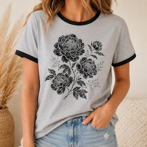 May include: Gray t-shirt with black trim featuring a black floral design. The graphic includes three large peony blooms and delicate foliage. The shirt is paired with denim shorts.