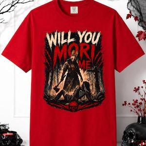 Può includere: Una t-shirt rossa a maniche corte con una stampa grafica di una figura mascherata che tiene un'ascia sopra una persona a terra in una foresta oscura. Il testo "WILL YOU MORI ME" è stampato in grandi lettere bianche e rosse dall'aspetto usurato.