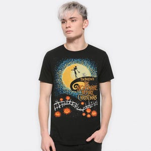 Może przedstawiać: Czarny t-shirt z grafiką z filmu Tima Burtona "Miasteczko Halloween". Projekt zawiera sylwetkę Jacka Skellingtona na wzg&oacute;rzu, pełnię księżyca i tytuł filmu. Pomarańczowe dynie i płot znajdują się na dole.