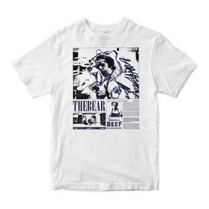 May include: A white short-sleeve t-shirt featuring a graphic print with a black and white photograph of a person wearing a bear headpiece. The design includes the text THE BEAR, THE ORIGINAL BEEF OF CHICAGOLAND, and additional small printed text.