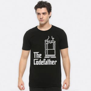 May include: Black t-shirt with a white graphic. The graphic features a laptop suspended by binary code chains, with the text "The Codefather" below. The shirt is short-sleeved and made of a soft material.