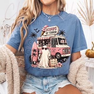 May include: Pale blue t-shirt with a pink ice cream van graphic, reading "SCOOPS OF TERROR". A ghost with sunglasses holds an ice cream and gives a peace sign. The design has a spooky, beach theme.