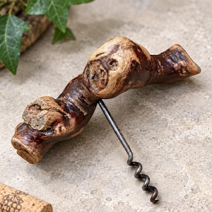 Könnte beinhalten: Ein Korkenzieher mit einem Griff aus einem Stück natürlichem, poliertem braunem Holz mit einer ausgeprägten knorrigen Textur. Eine metallische, spiralförmige Spindel ist in der Mitte des Holzgriffs befestigt und ragt nach unten heraus.