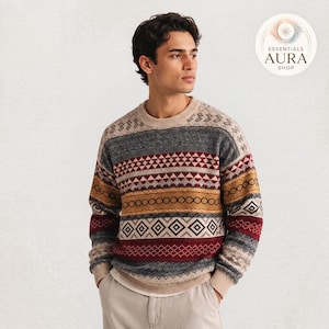 May include: A long-sleeve crewneck sweater featuring a multi-colored geometric pattern in shades of red, gold, gray, and cream. The design includes horizontal bands of diamonds, triangles, and circles. A logo reads ESSENTIALS AURA SHOP.