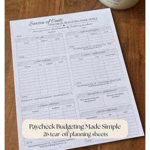 May include: A white paper budgeting sheet titled Season of Cents Paycheck Budgeting Made Simple with sections for income, fixed and variable expenses, extra debt payments, savings, and cash denominations, featuring 26 tear-off planning sheets.