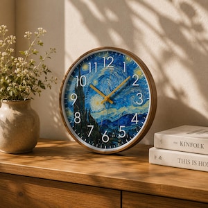 May include: Round wall clock with a wooden frame. The clock face features a blue and yellow starry night design, with black numbers and yellow clock hands. The clock is displayed on a wooden surface.