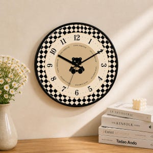 May include: A round wall clock with a black and white checkered border. The clock face is beige with black numbers and hands. A black teddy bear graphic is in the center. The words "LOVE FOREVER" are printed around the clock face.