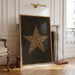 May include: A framed art print featuring a large star with a leopard print pattern on a black background. The artwork is displayed in a room with a vintage chair, a fireplace, and a window. The frame is made of wood.
