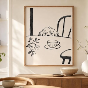 May include: A framed art print featuring a whimsical illustration of a dog peeking over a table. The black and white drawing includes a teacup, chair, and floral accents. The artwork is displayed in a room with a wooden cabinet and a white vase.