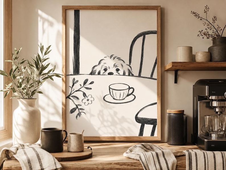 May include: A framed black and white illustration depicts a dog peeking over a table set for tea. A teacup and saucer are on the table. The scene is in a kitchen with a coffee maker, mugs, and a vase with greenery.