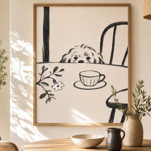 May include: A framed black and white illustration of a dog peeking over a table with a teacup and saucer. The artwork is in a wooden frame and is displayed in a room with a table, vase, and other decor.