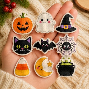 May include: A collection of nine small Halloween-themed cross-stitch patches featuring an orange pumpkin, a white ghost, a black witch hat, a black cat, a black bat, a spider on a web, candy corn, a yellow crescent moon, and a black cauldron.