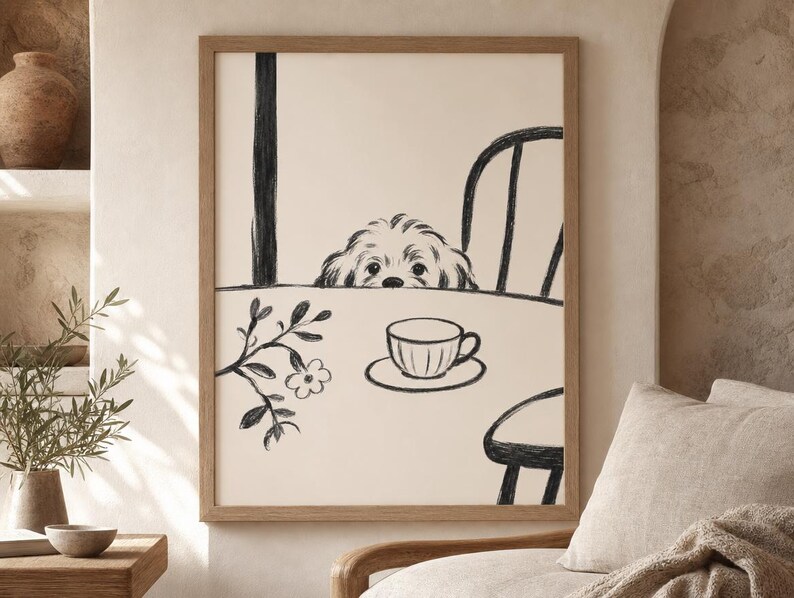 May include: A framed black and white illustration of a dog peeking over a table with a teacup and saucer. The artwork has a minimalist style, with a dog, chair, and floral branch. The frame is a light brown color.